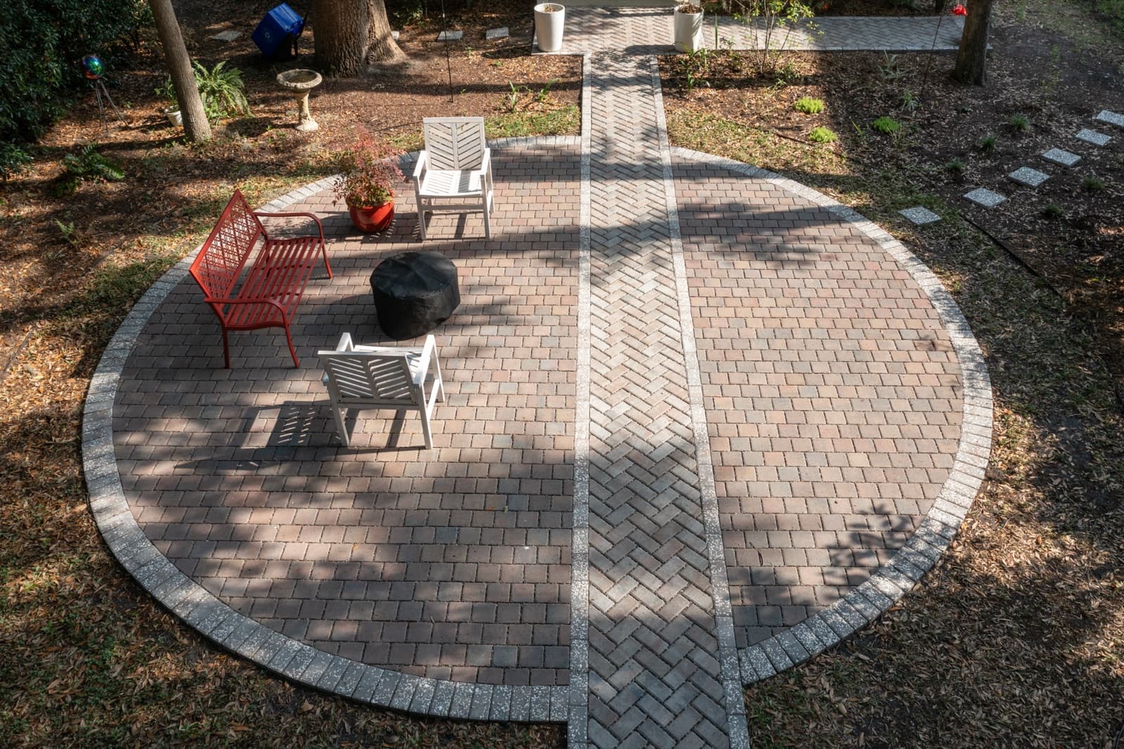 Aerial view of a circular herringbone paver patio with a contrasting border, connected to the home by a straight paver path, under live oaks in Port Royal, SC
