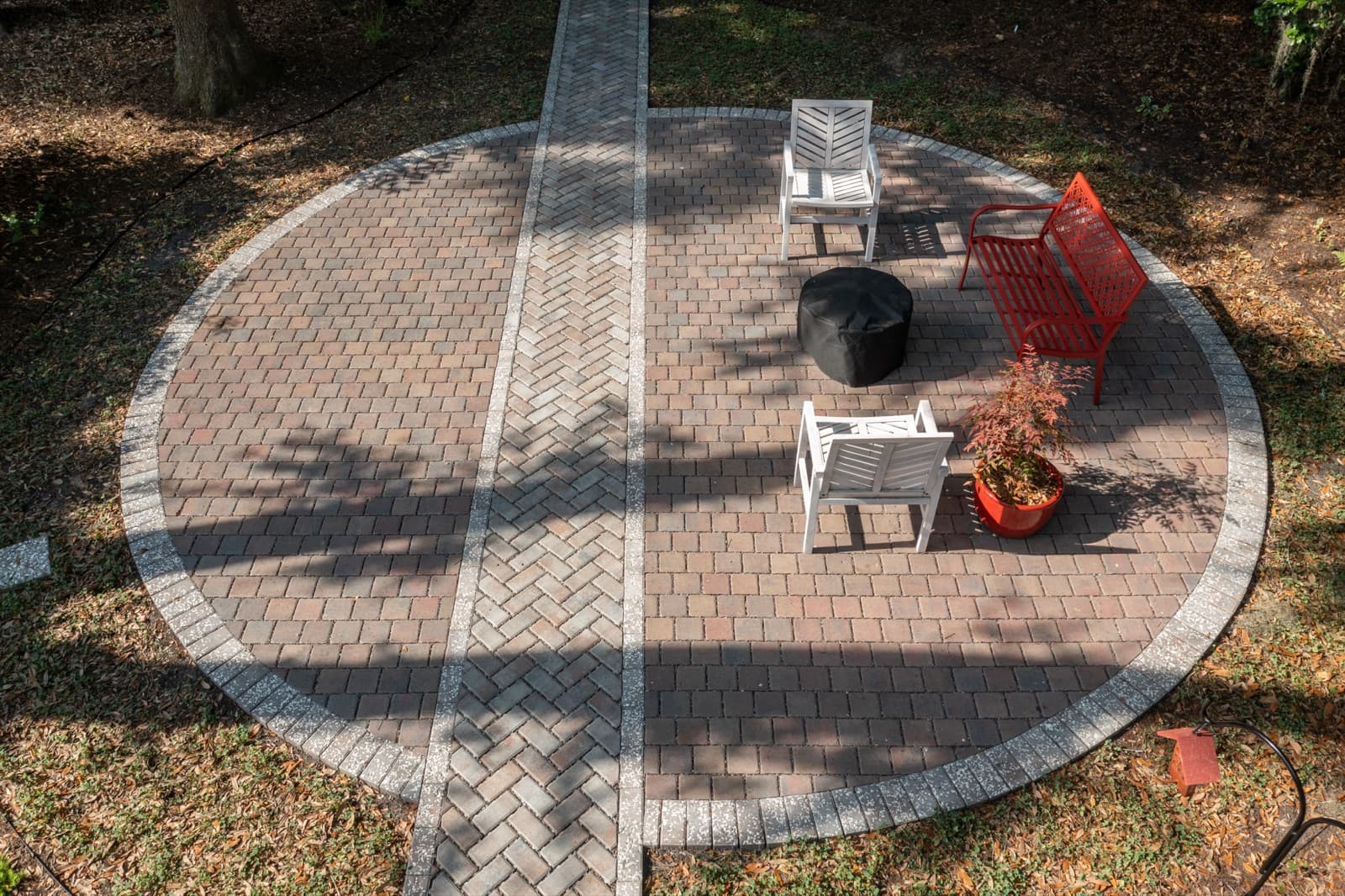 Circular paver patio with seating and a fire bowl, viewed from above under the tree canopy