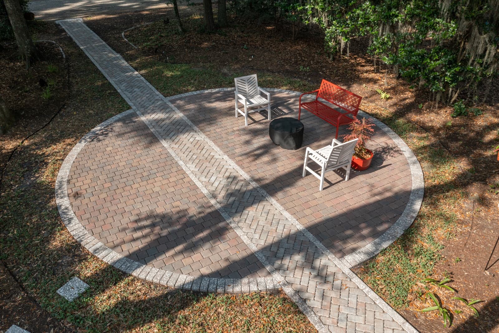 Circular patio with white chairs, a red bench, and a fire bowl surrounded by dappled shade