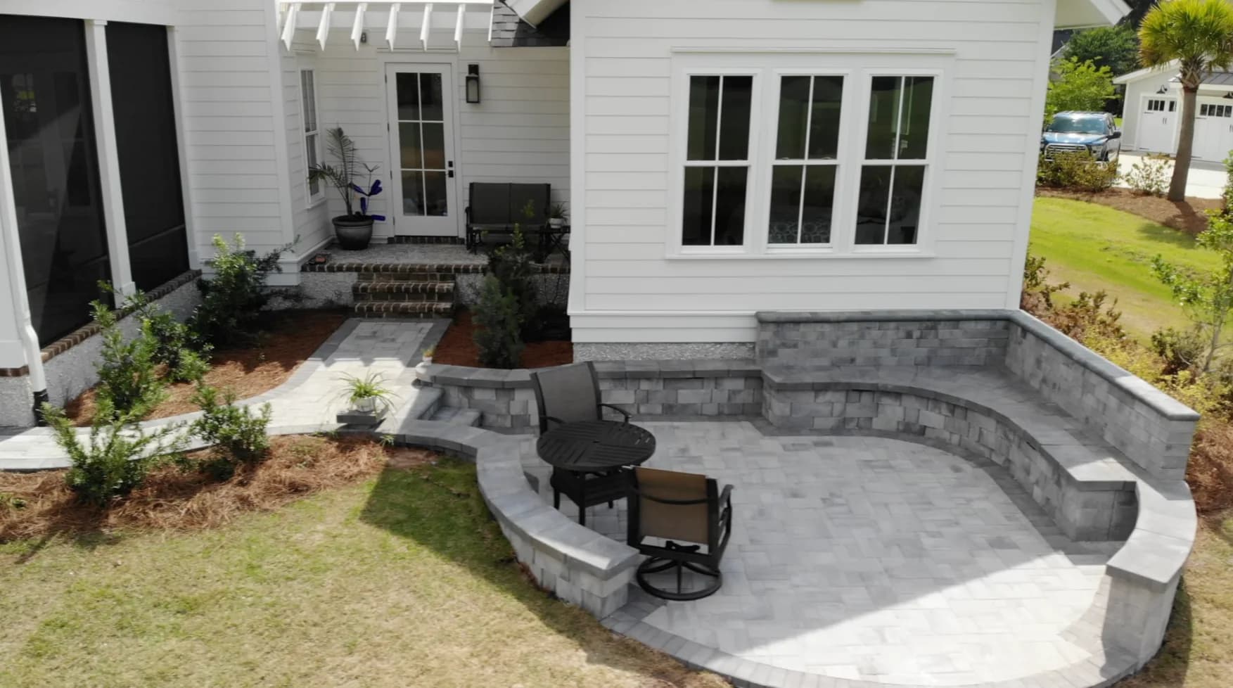 Finished overview of the connected paver patio zones and curved sitting wall behind the Hampton Hall home