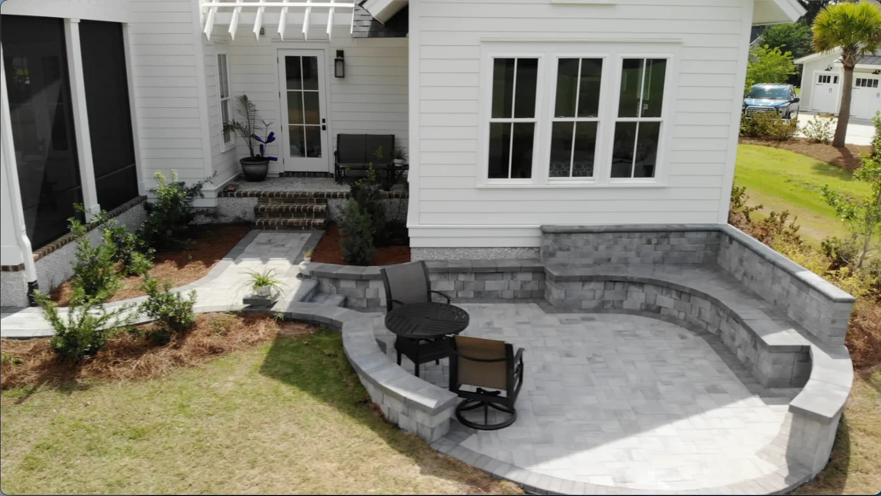 Finished light-gray paver patio with a curved sitting wall and a second connected gathering area at a waterfront Hampton Hall home in Bluffton, SC