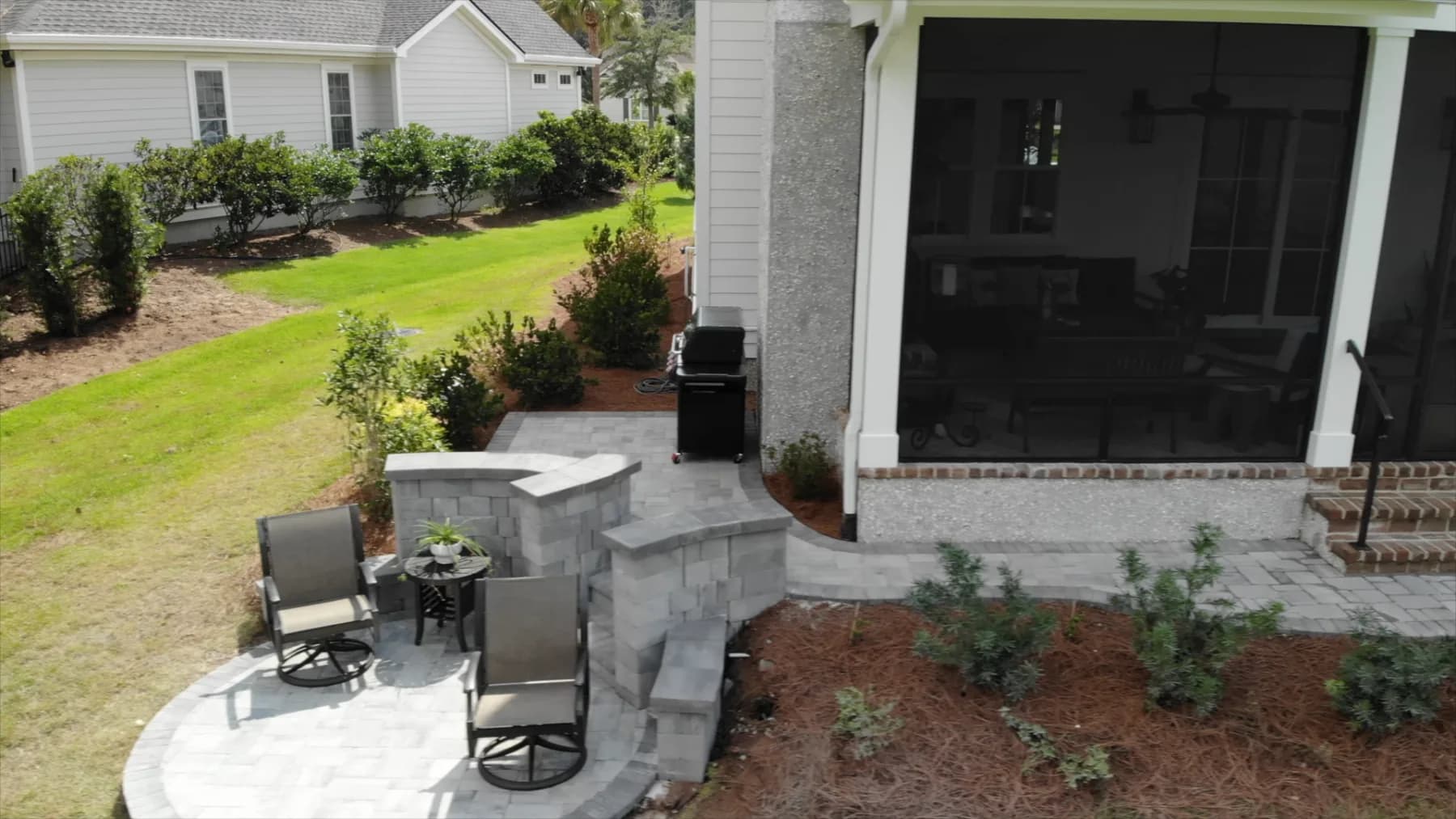 Finished curved paver sitting wall with chairs beside the screened porch and restored landscaping