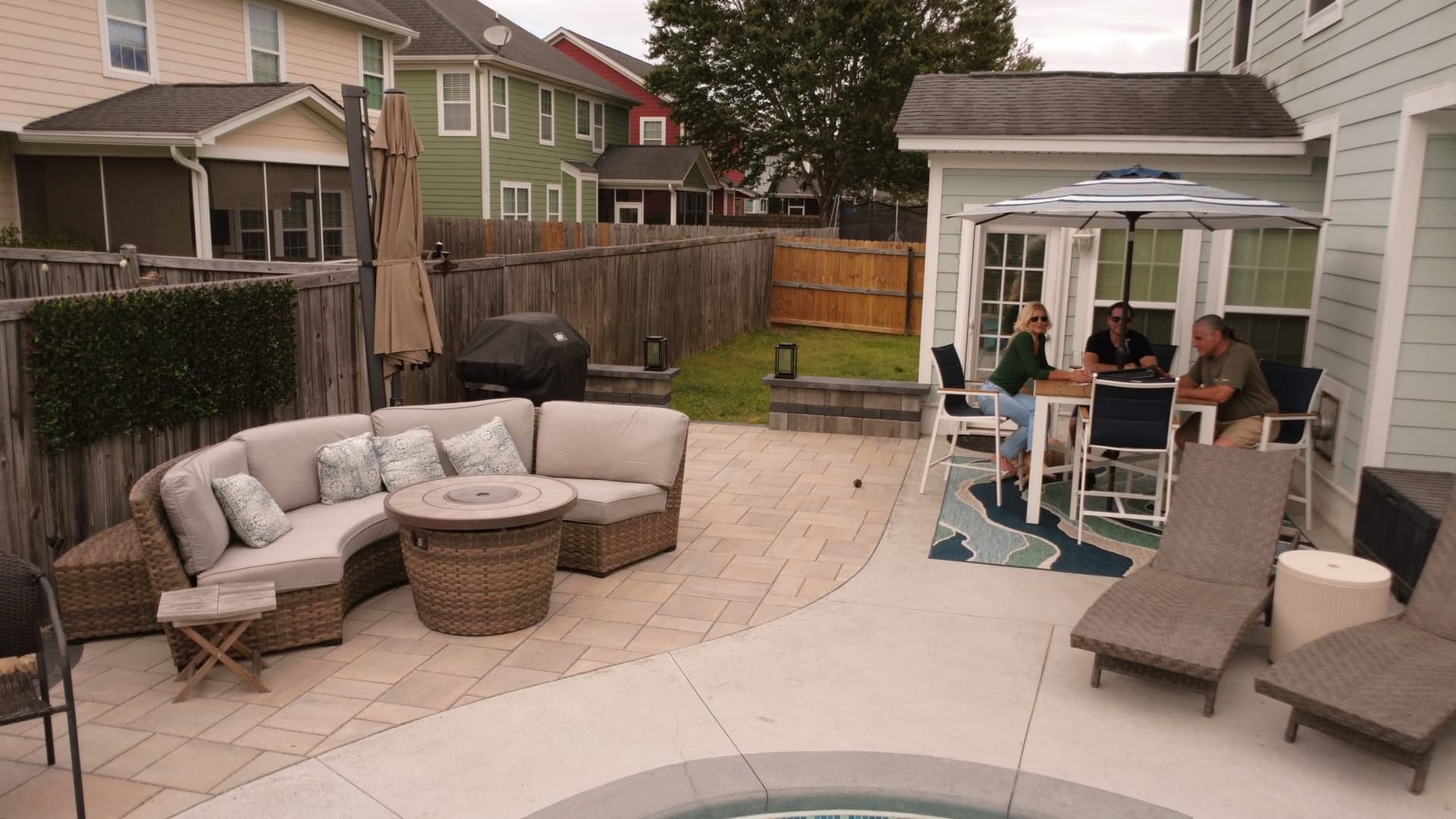 Homeowners relaxing on the new paver pool deck with a fire-pit lounge and dining set