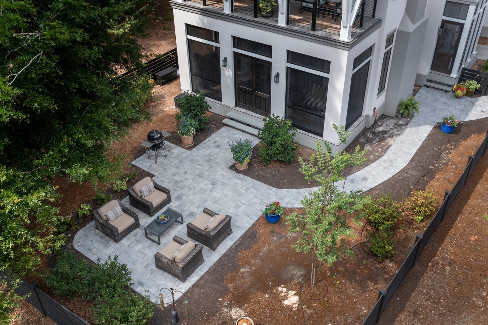 Light-grey paver patio with modern lounge furniture and a winding paver path beside a contemporary coastal home on Cat Island, Beaufort, SC