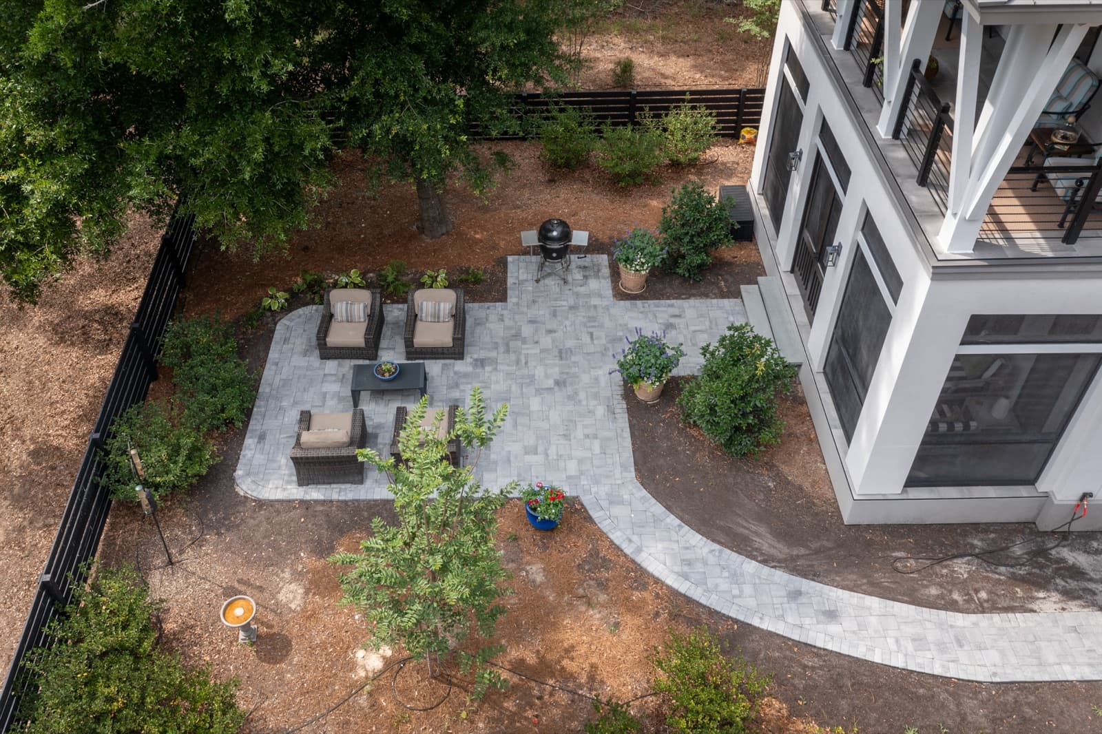 Light-grey paver patio with potted plants and young crepe myrtles