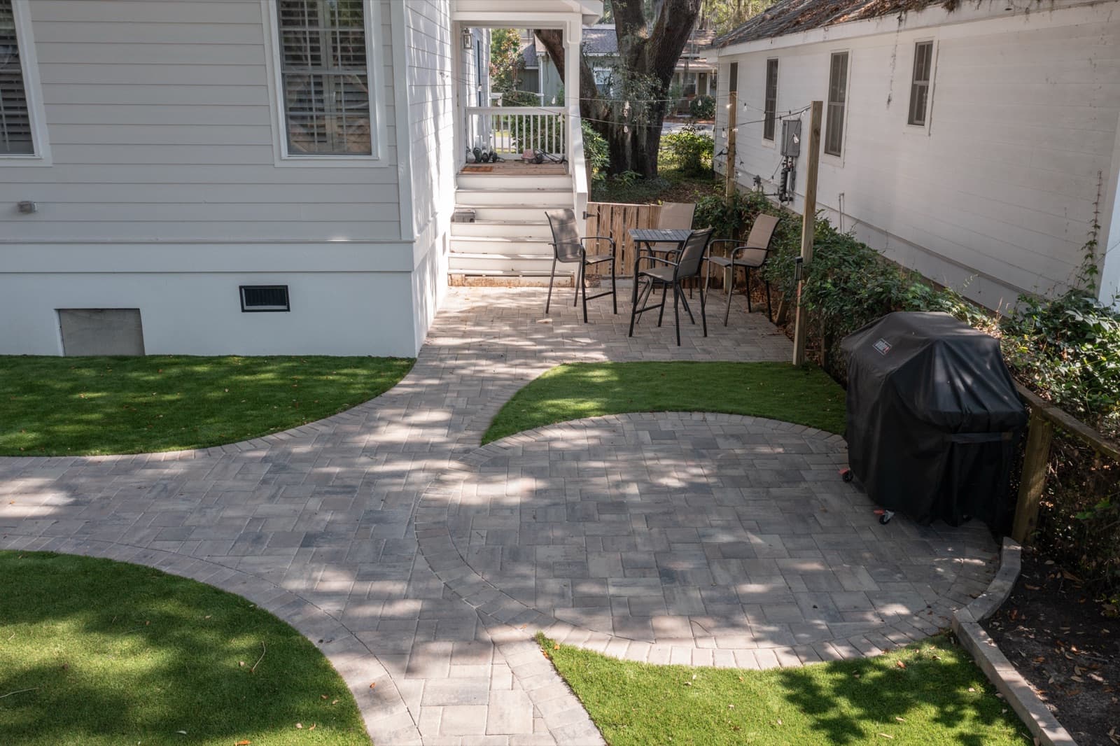 Curving paver path threading between turf panels under the oak canopy