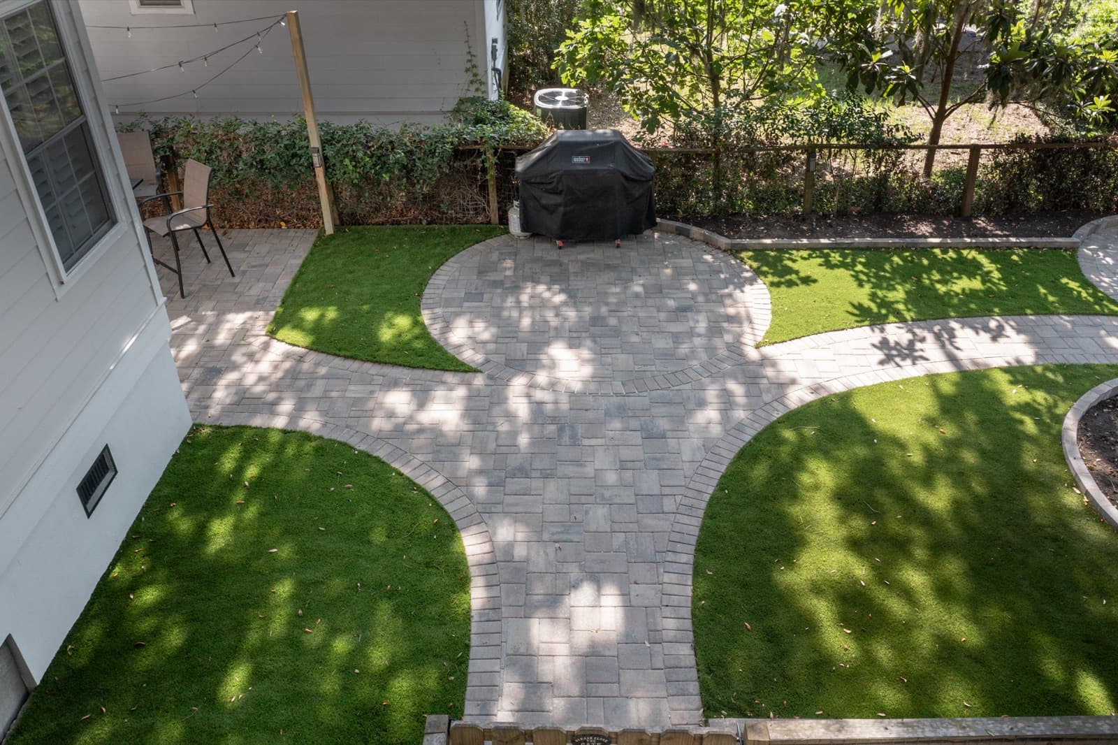 Herringbone paver patio meeting clean artificial turf in the shaded backyard