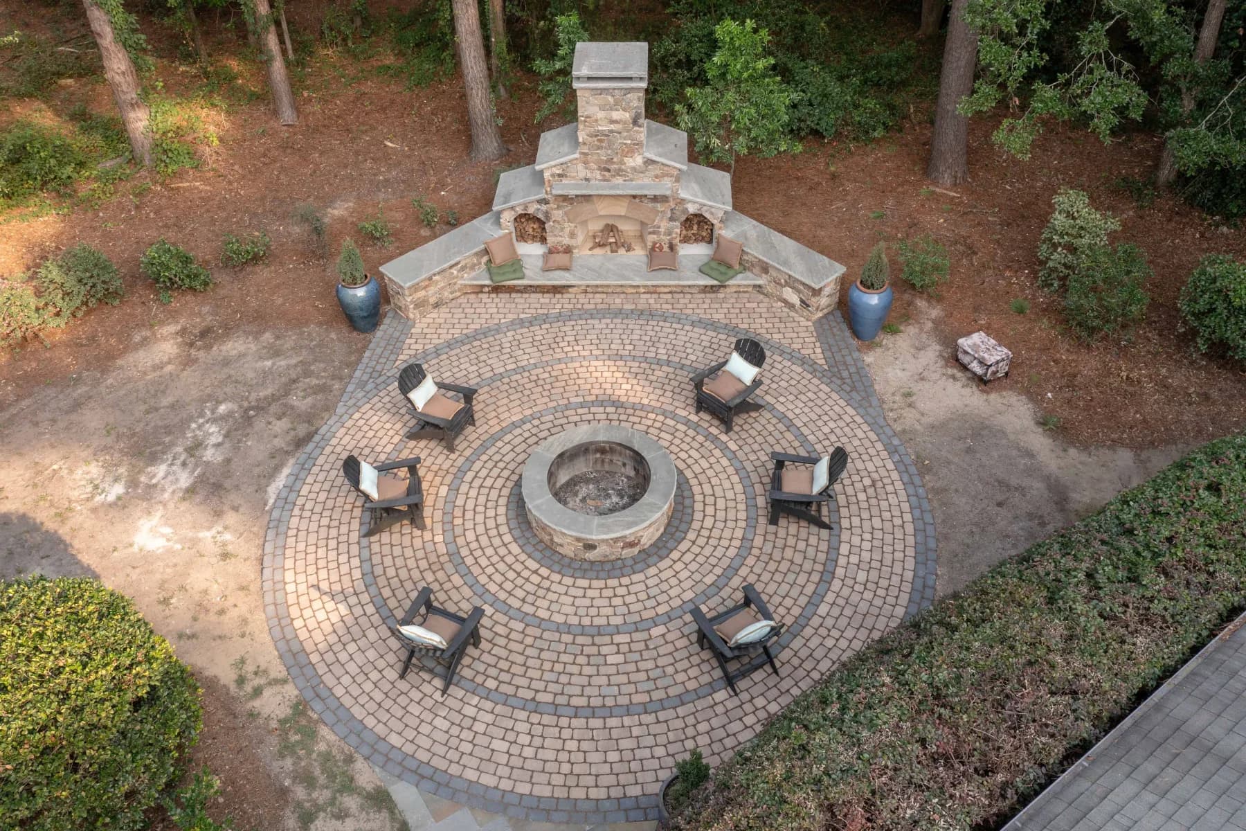 Circular paver patio with Adirondack chairs, central fire pit, and stone outdoor fireplace